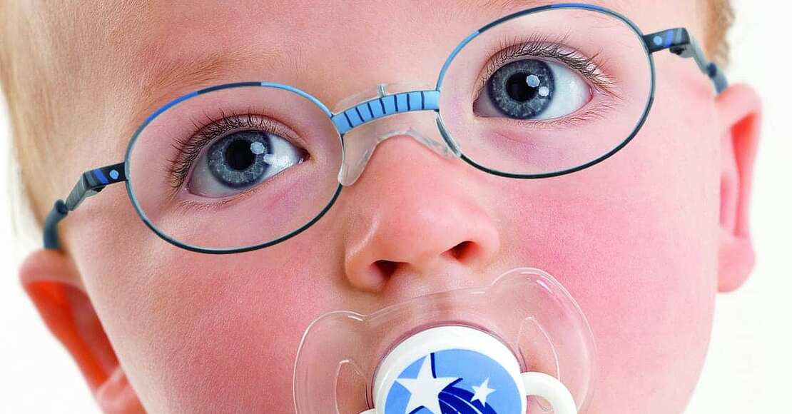 Ein in die Kamera schauendes Baby trägt aufgrund einer Sehschwäche eine blaue Babybrille