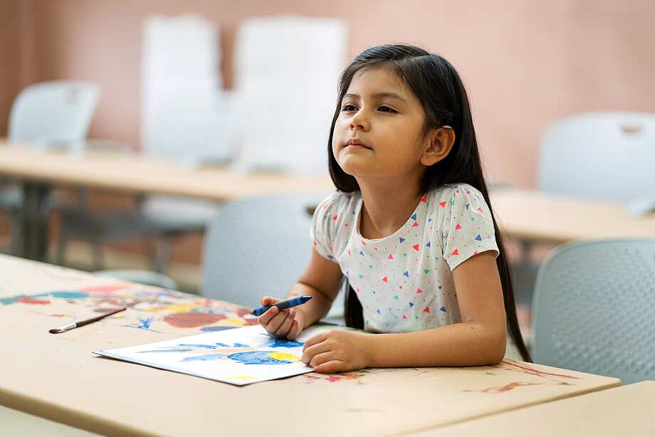 Anzeichen für Kurzsichtigkeit bei Kindern: Mädchen kneift Augen beim Lesen in der Schule zusammen