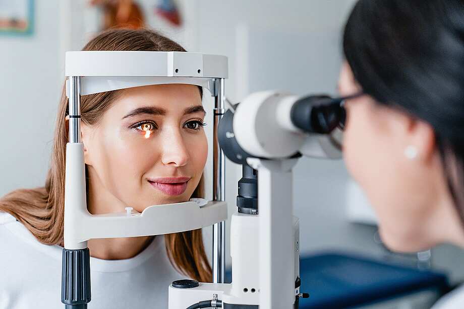Eine Optikerin führt mithilfe einer Spaltlampe einen Sehtest bei einer jungen Erwachsenen durch
