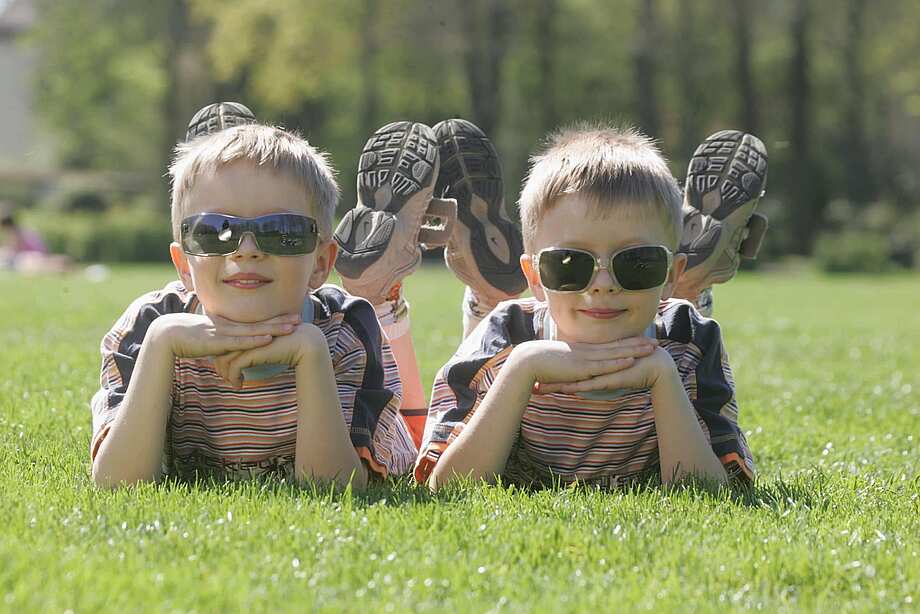 Zwei Jungen liegen auf einer Wiese und tragen Kindersonnenbrillen