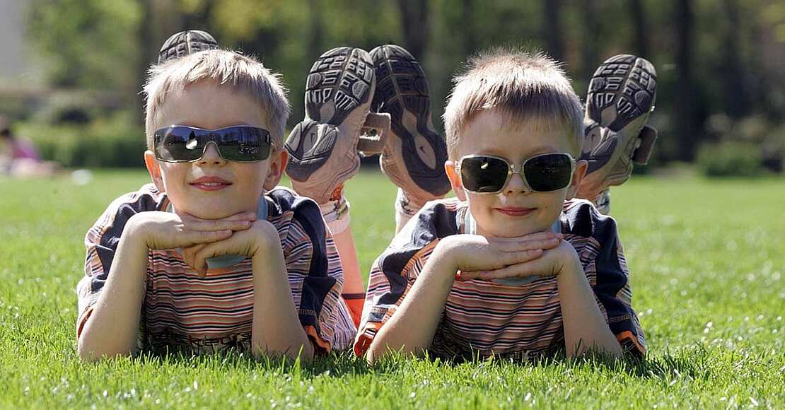 Zwei Kinder mit Sonnenbrillen liegen im Sommer auf einer Wiese