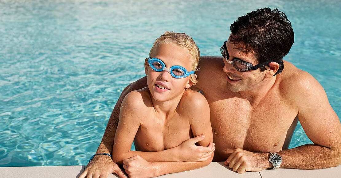 Vater und Sohn mit Schwimmbrillen am Beckenrand